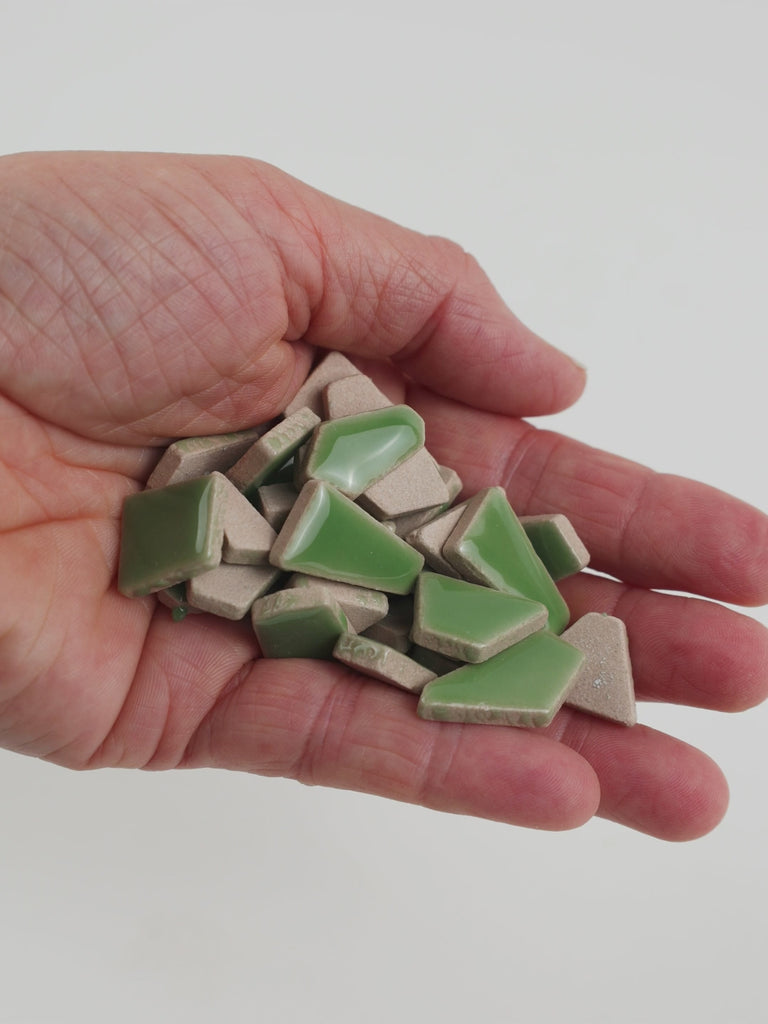 Video of Flip ceramic puzzle pieces in reed green, opaque glazed porcelain, 4–20 mm, held in a hand and poured out to show their shapes and finish