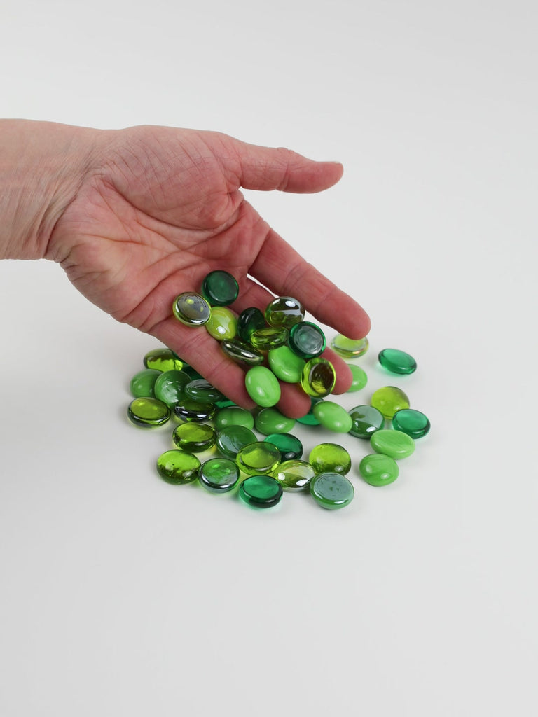 Video of green mix glass nuggets in lime, grass and emerald green shades with an iridescent sheen, 16–20 mm, picked up from a pile by hand and dropped back to show their size, round shape and shine