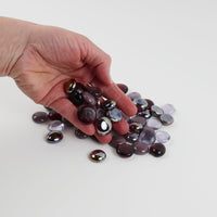 Video of purple mix glass nuggets in aubergine, plum and lilac shades with an iridescent sheen, 16–20 mm, picked up from a pile by hand and dropped back to show their size, round shape and shine