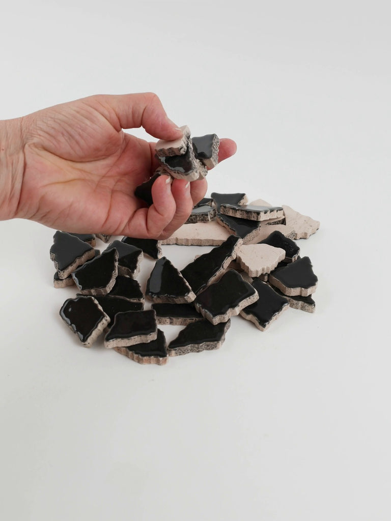 Video of Flip XL ceramic puzzle pieces in anthracite, opaque glazed porcelain, 20–60 mm, picked up from a pile by hand and dropped back to show their size, shapes and finish