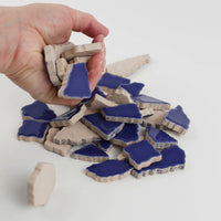 Video of Flip XL ceramic puzzle pieces in cobalt, opaque glazed porcelain, 20–60 mm, picked up from a pile by hand and dropped back to show their size, shapes and finish
