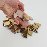 Video of Flip XL ceramic puzzle pieces in gold, opaque glazed porcelain, 20–60 mm, picked up from a pile by hand and dropped back to show their size, shapes and finish